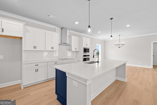 kitchen featuring an island with sink, sink, white cabinets, wall chimney exhaust hood, and pendant lighting