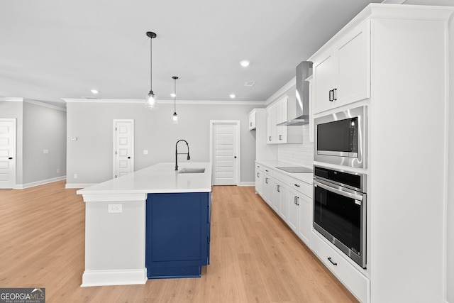 kitchen featuring a center island with sink, sink, decorative light fixtures, wall chimney range hood, and stainless steel appliances