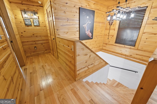 staircase featuring hardwood / wood-style floors, an inviting chandelier, and wooden walls