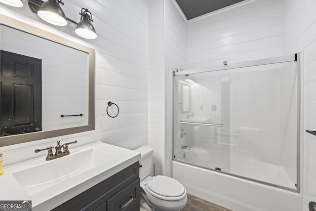 full bathroom with bath / shower combo with glass door, toilet, wood walls, and vanity