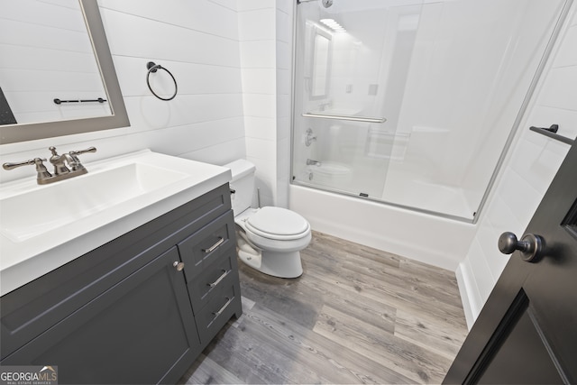 full bathroom with vanity, wooden walls, toilet, hardwood / wood-style flooring, and combined bath / shower with glass door