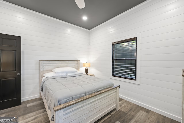 bedroom with ceiling fan, dark hardwood / wood-style flooring, and wooden walls