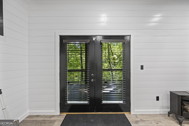 doorway featuring light wood-type flooring, wooden walls, and french doors