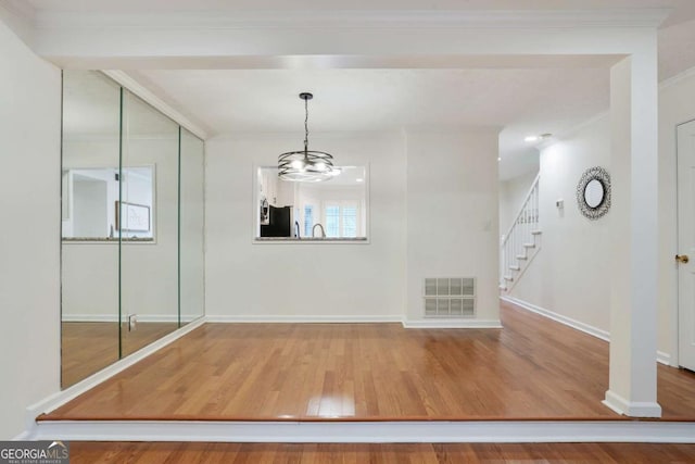 unfurnished dining area with hardwood / wood-style flooring, ornamental molding, and an inviting chandelier