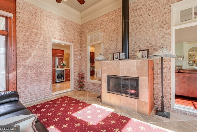 unfurnished living room featuring ceiling fan, a high ceiling, light tile patterned floors, and a tile fireplace