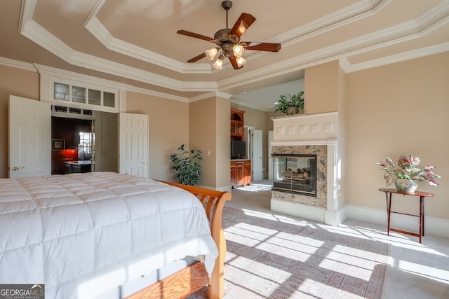 carpeted bedroom featuring ceiling fan, a high end fireplace, ornamental molding, and a tray ceiling