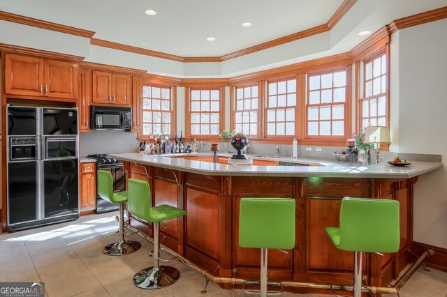 kitchen with crown molding, kitchen peninsula, light tile patterned flooring, black appliances, and a breakfast bar area