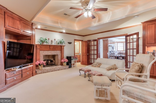 living room featuring carpet floors, ceiling fan, a brick fireplace, a tray ceiling, and crown molding