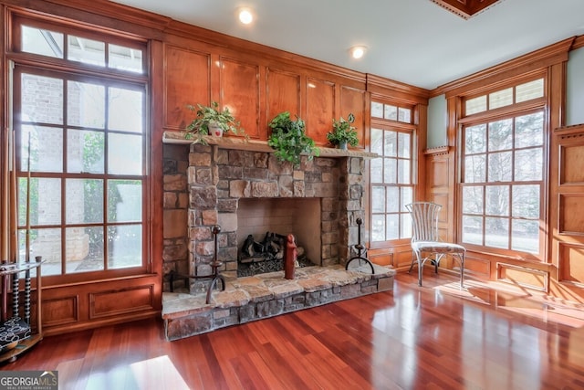 sitting room with a wealth of natural light, a stone fireplace, and wood-type flooring