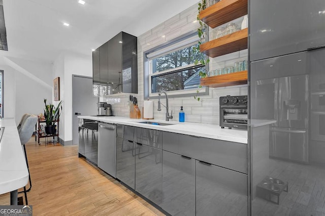 kitchen featuring tasteful backsplash, dishwasher, sink, and light wood-type flooring