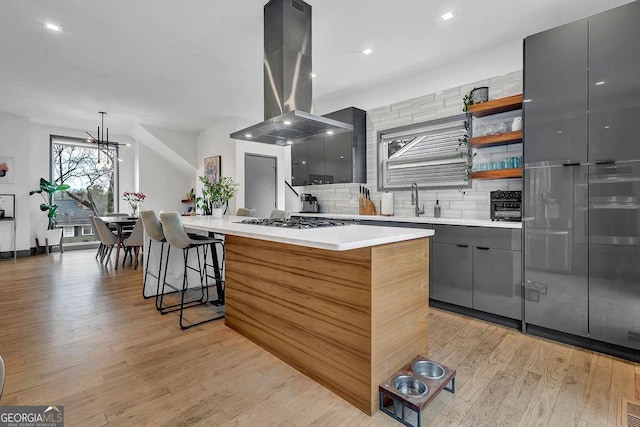 kitchen featuring island range hood, gray cabinetry, backsplash, a center island, and light hardwood / wood-style flooring