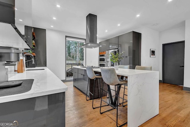 kitchen featuring island exhaust hood, stainless steel appliances, a kitchen breakfast bar, and light hardwood / wood-style floors