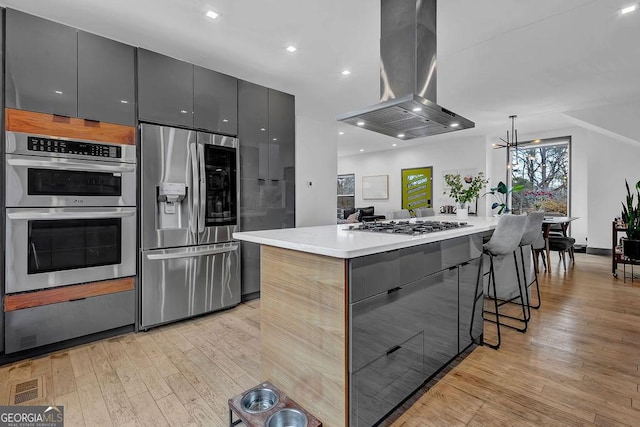 kitchen featuring gray cabinets, island range hood, decorative light fixtures, stainless steel appliances, and a spacious island