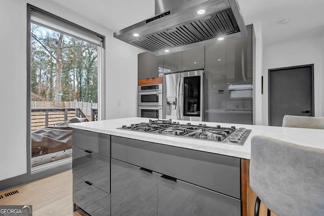 kitchen with a kitchen bar, ventilation hood, light hardwood / wood-style flooring, appliances with stainless steel finishes, and gray cabinets