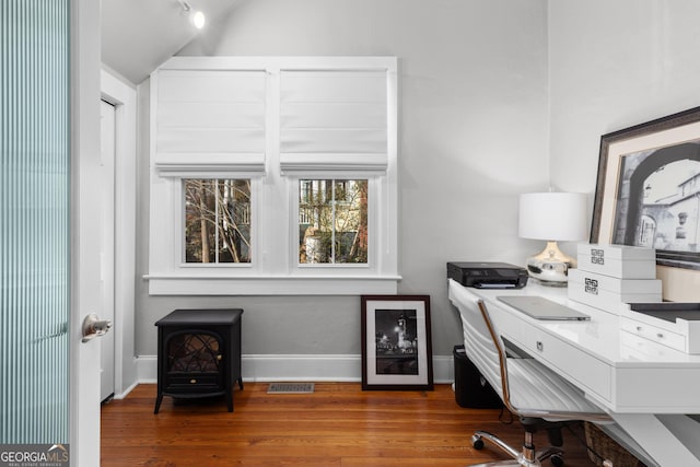 office area with wood-type flooring, lofted ceiling, and a wood stove