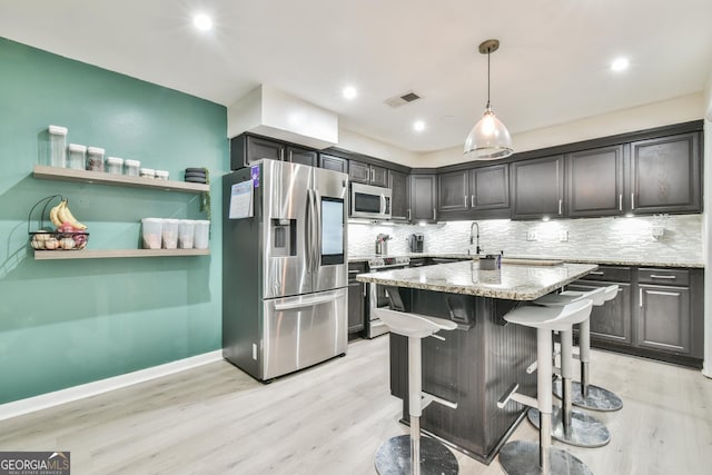 kitchen with a breakfast bar area, appliances with stainless steel finishes, light stone countertops, light hardwood / wood-style floors, and decorative light fixtures