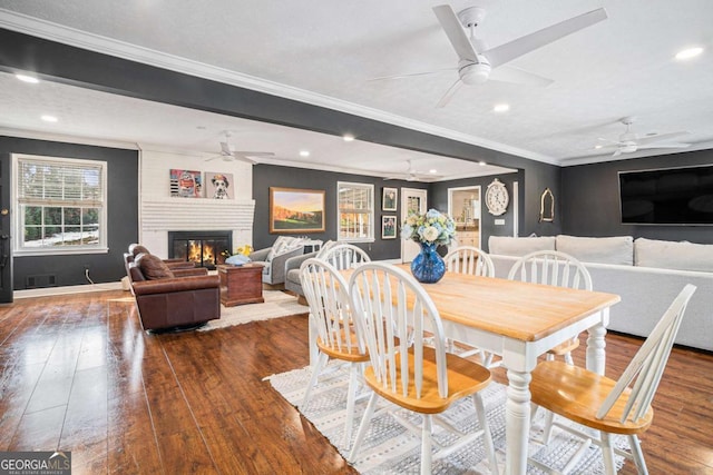 dining room featuring crown molding, dark hardwood / wood-style floors, a large fireplace, and ceiling fan