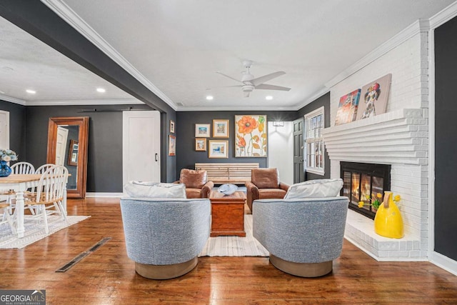 living room featuring ceiling fan, ornamental molding, a brick fireplace, and hardwood / wood-style floors