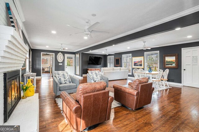 living room with crown molding, a brick fireplace, wood-type flooring, and ceiling fan