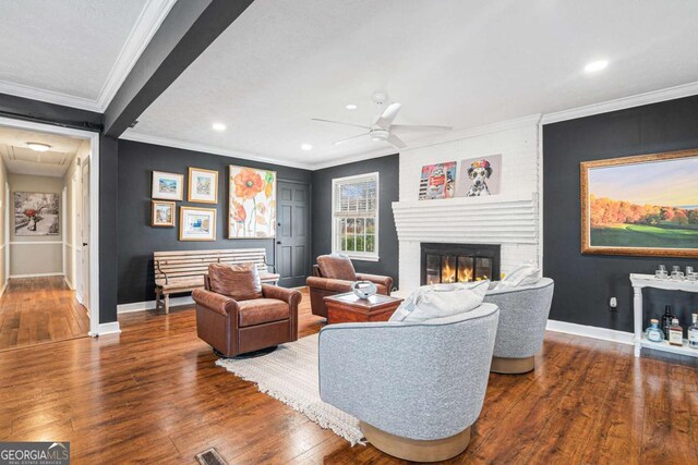 living room featuring a brick fireplace, ornamental molding, dark hardwood / wood-style floors, and ceiling fan