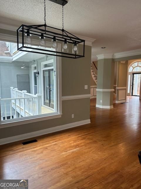 unfurnished dining area featuring wood-type flooring, ornamental molding, and a textured ceiling