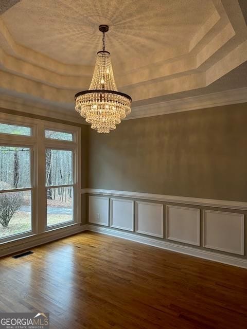 unfurnished dining area featuring a notable chandelier, a tray ceiling, ornamental molding, and hardwood / wood-style flooring