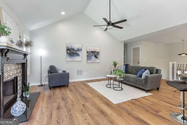 living room with ceiling fan, high vaulted ceiling, hardwood / wood-style floors, and a tiled fireplace