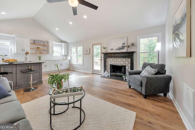 living room with light wood-type flooring, high vaulted ceiling, a healthy amount of sunlight, and a tile fireplace