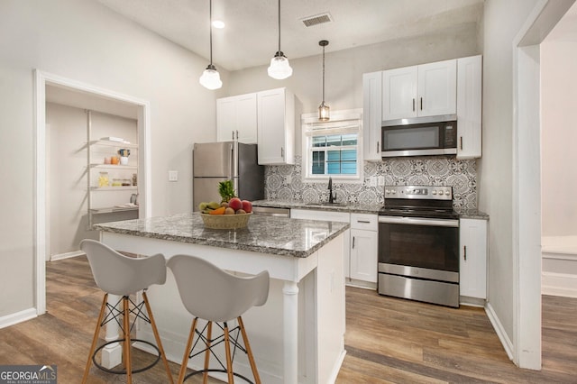 kitchen with white cabinets, dark stone counters, a center island, dark hardwood / wood-style floors, and stainless steel appliances