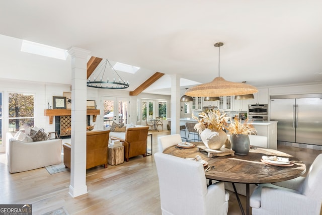 dining area featuring french doors, a skylight, light hardwood / wood-style floors, and decorative columns