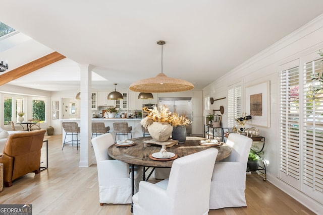 dining space featuring beamed ceiling, decorative columns, and light wood-type flooring