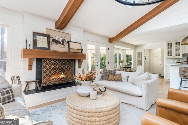 living room with a large fireplace, beamed ceiling, and french doors