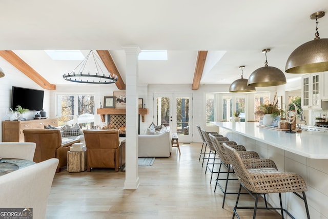 living room featuring light hardwood / wood-style floors, french doors, beamed ceiling, and ornate columns