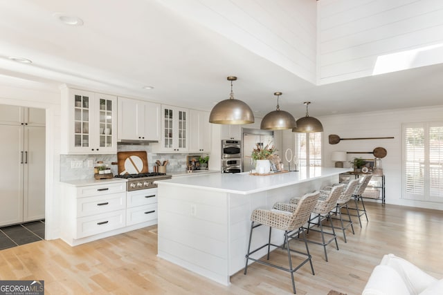 kitchen featuring a breakfast bar area, white cabinetry, decorative light fixtures, a large island with sink, and stainless steel appliances