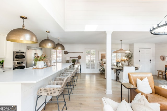 kitchen with appliances with stainless steel finishes, decorative light fixtures, decorative columns, white cabinetry, and light hardwood / wood-style floors