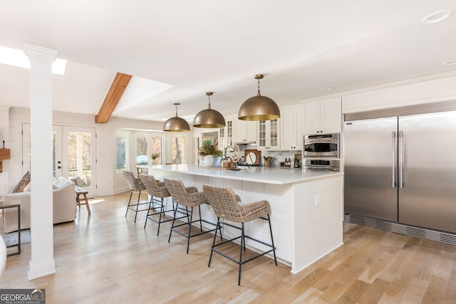 kitchen featuring ornate columns, appliances with stainless steel finishes, pendant lighting, decorative backsplash, and a large island