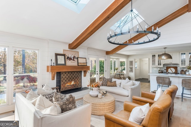 living room featuring a chandelier, vaulted ceiling with skylight, light wood-type flooring, and french doors