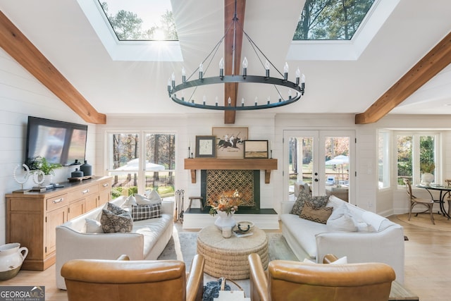 living room featuring a skylight, beamed ceiling, a notable chandelier, light wood-type flooring, and french doors