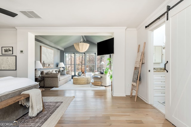 bedroom with connected bathroom, crown molding, vaulted ceiling, a barn door, and light hardwood / wood-style floors