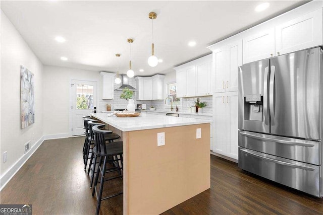 kitchen featuring white cabinets, a center island, backsplash, hanging light fixtures, and stainless steel fridge