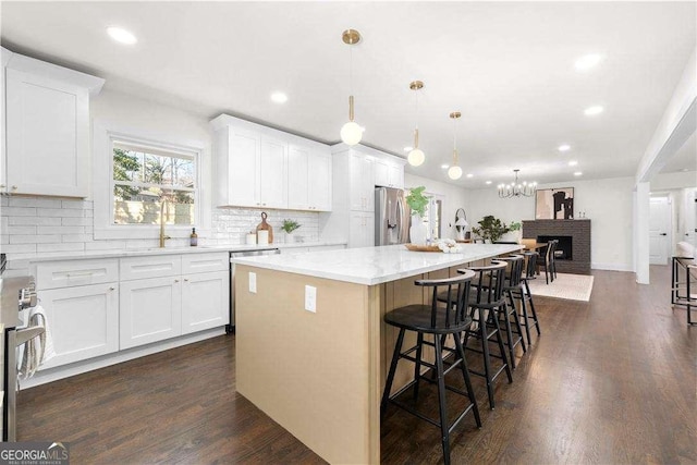 kitchen featuring a center island, a kitchen bar, appliances with stainless steel finishes, white cabinetry, and hanging light fixtures