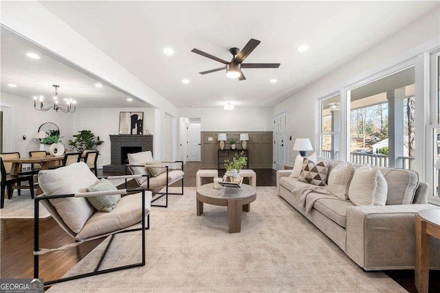 living room with ceiling fan with notable chandelier, light hardwood / wood-style flooring, and a fireplace