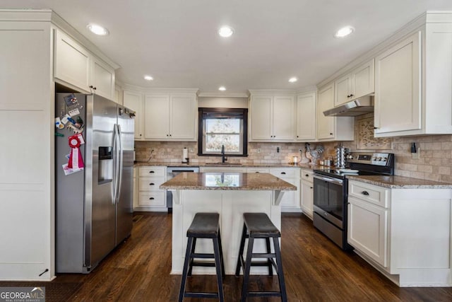 kitchen with appliances with stainless steel finishes, sink, white cabinetry, light stone countertops, and a kitchen island