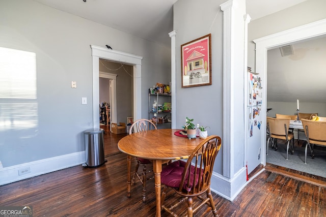 dining space featuring decorative columns, vaulted ceiling, and dark hardwood / wood-style flooring