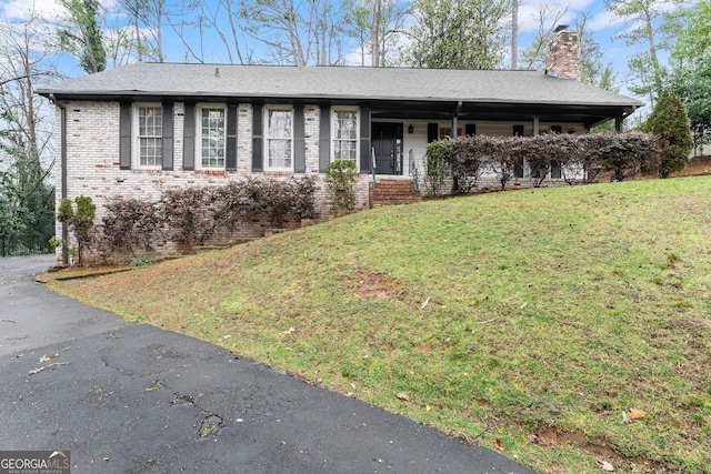 ranch-style house with brick siding, a shingled roof, a front yard, and a chimney