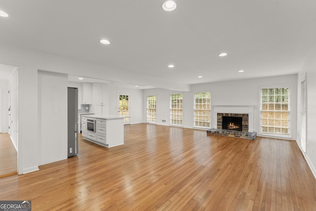 unfurnished living room featuring baseboards, light wood-type flooring, recessed lighting, and a brick fireplace