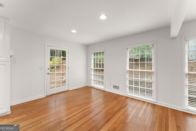 empty room featuring plenty of natural light, visible vents, and light wood-style floors