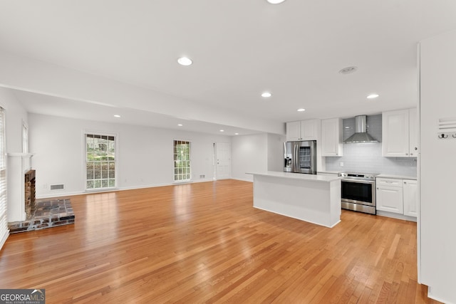 kitchen with wall chimney exhaust hood, open floor plan, light countertops, white cabinetry, and stainless steel appliances