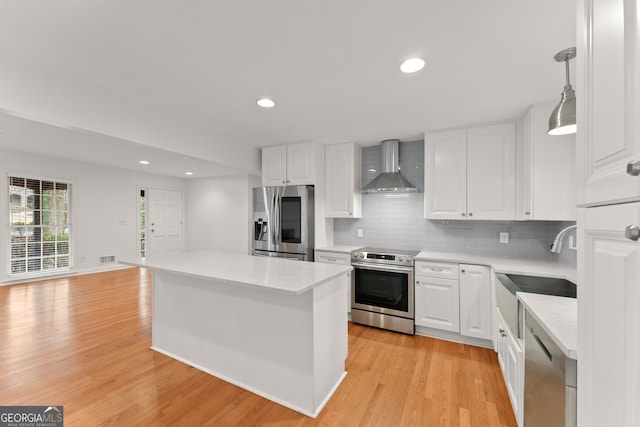 kitchen with a kitchen island, white cabinetry, wall chimney exhaust hood, decorative light fixtures, and stainless steel appliances