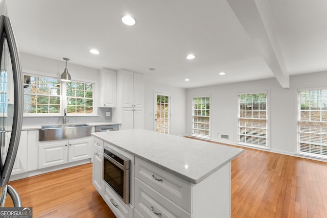 kitchen with hanging light fixtures, a kitchen island, white cabinetry, and a sink